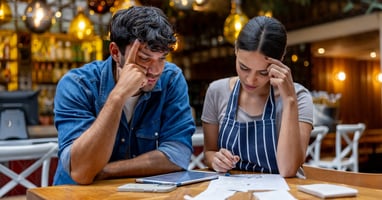 Two small business owners calculate bank holiday entitlement for part-time workers while reviewing paperwork at a restaurant table.