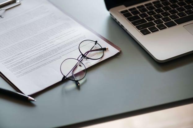 Contract with glasses and a laptop on a grey desk-min