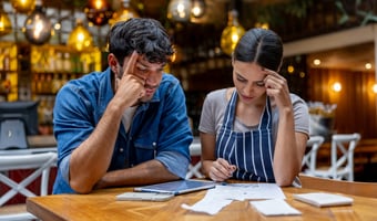 Two small business owners calculate bank holiday entitlement for part-time workers while reviewing paperwork at a restaurant table.