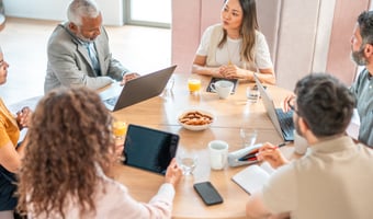 Group of colleagues sitting around a table in an office, reviewing documents and discussing how to select employees for redundancy using fair and objective criteria.