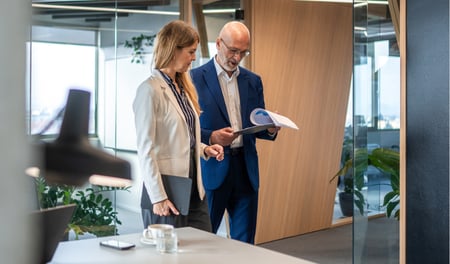 Two workers are walking through an office space with a clipboard, performing a risk assessment for their small business. 