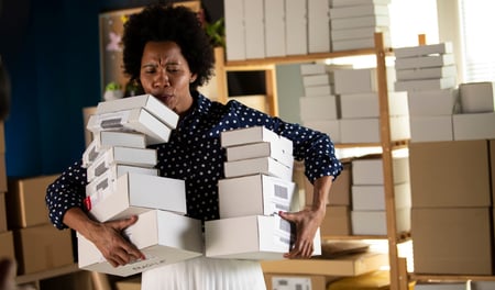 An office worker struggles to hold several boxes in each hand which could result in the need to report an incident or near miss at work. 