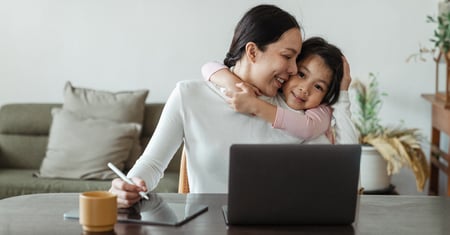 Parent working from home on a laptop while hugging their child, illustrating flexible working for parents and carers in SMEs.