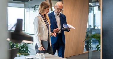 Two workers are walking through an office space with a clipboard, performing a risk assessment for their small business. 