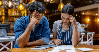 Two small business owners calculate bank holiday entitlement for part-time workers while reviewing paperwork at a restaurant table.