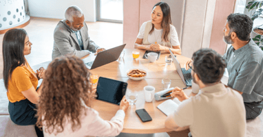 Group of colleagues sitting around a table in an office, reviewing documents and discussing how to select employees for redundancy using fair and objective criteria.