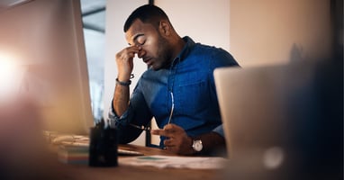 Stressed male employee with head in hand at his desk, showing the psychological impact of redundancy survivor syndrome on surviving employees.