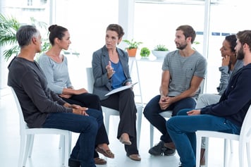 Colleagues are sitting on chairs in a circle and having a group therapy session to promote employee wellbeing.