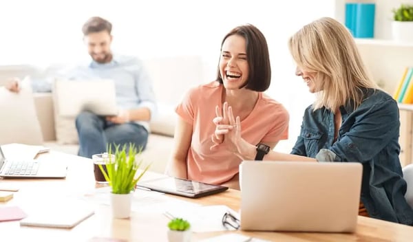 Two female employees laughing in the office-min