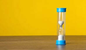 Sand timer on a table, with a bright yellow background 