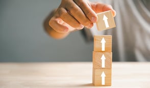 Wooden cubes are shown, with white upward-pointing arrows painted on them. Someone is stacking the cubes on top of each other, placing the 4th cube on the top.