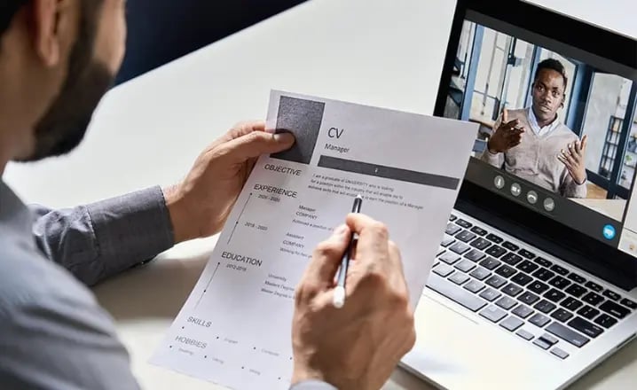 A man reviews a CV whilst the interviewee is on his laptop via video call