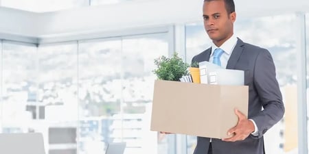 An employee is walking out the office holding a cardboard box. In the cardboard box is some of the man