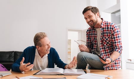 Two men are in conversation in an office environment. Their body language is relaxed and they