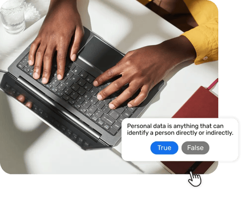 A person's hands shown typing on a laptop keyboard, photo taken from above desk, with a Breathe product pop up showing a true or false question from the GDPR course they are completing