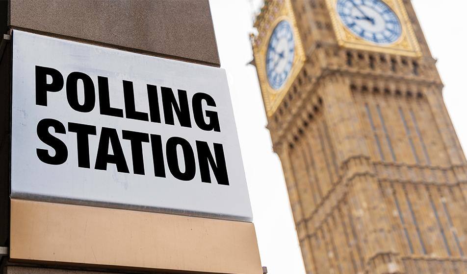 A polling station sign is shown next to Big Ben, the Elizabeth Tower clock of the Palace of Westminster, against a white overcast sky.