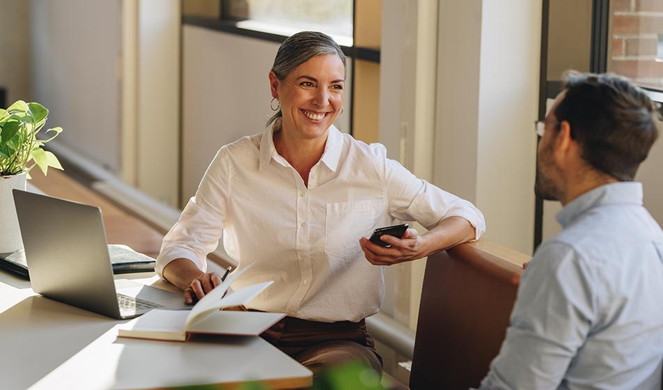 A woman and a man sit in an office environment, talking and smiling