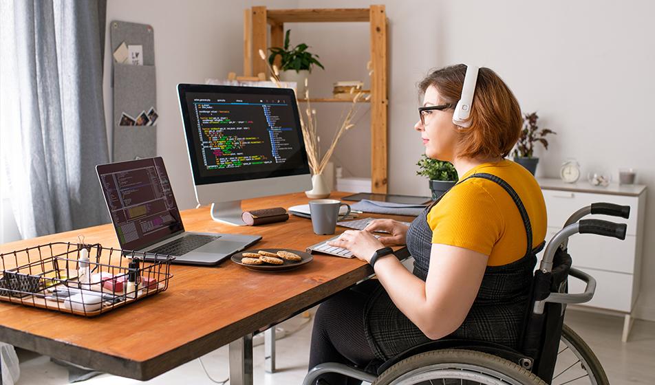 A woman in a wheelchair sits at her desk, working remotely from home. 