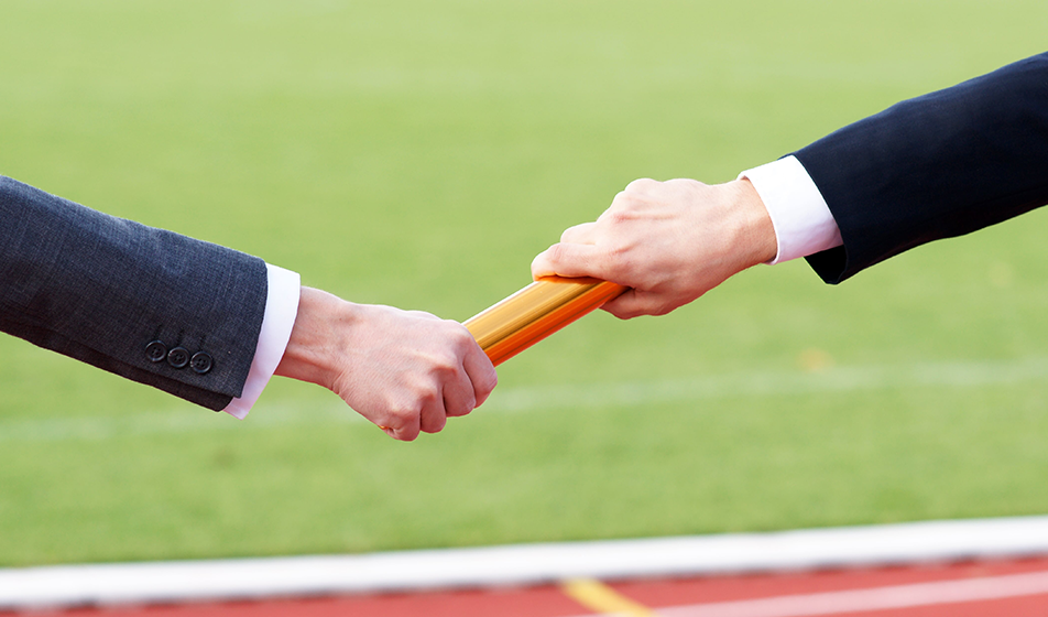 Someone wearing a suit, passing an orange baton to another person in a suit.