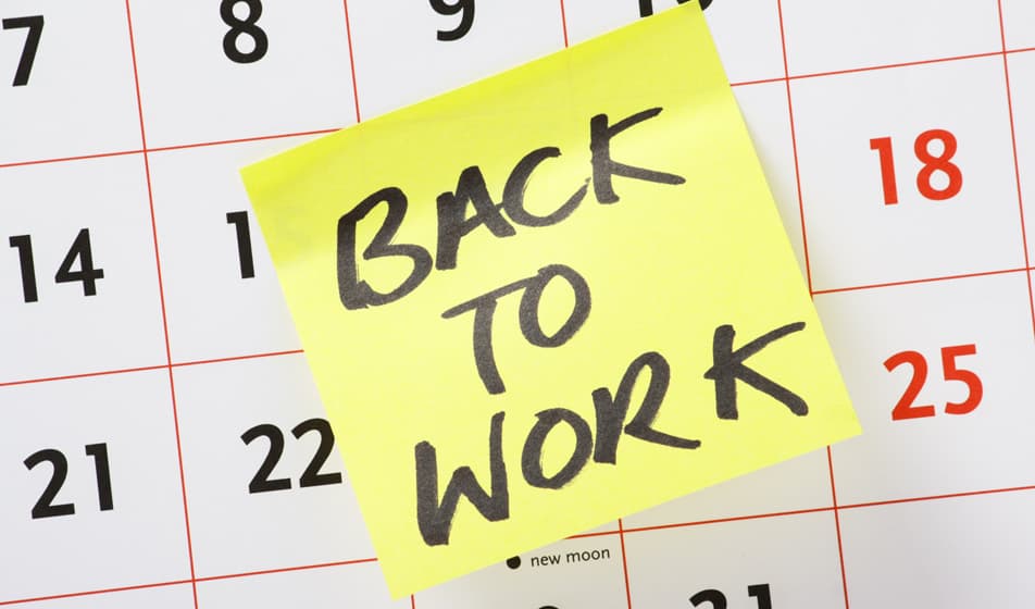 A yellow sticky note is stuck on a calendar with the words "back to work" on it.