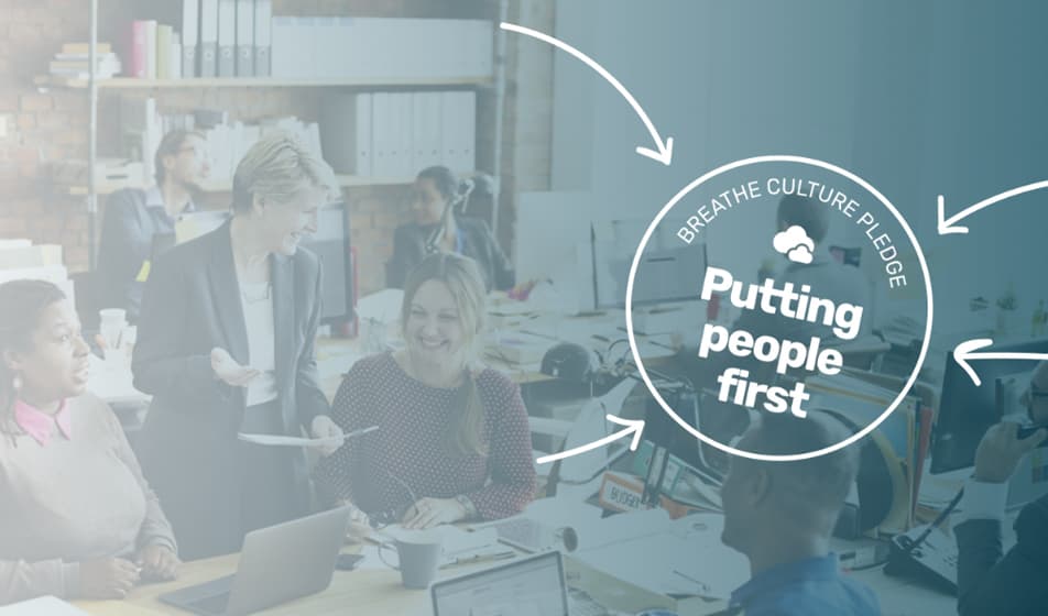 An image of people sat together within an office. Over the image is a circle stamp which says "Breathe Culture Pledge: Putting people first".