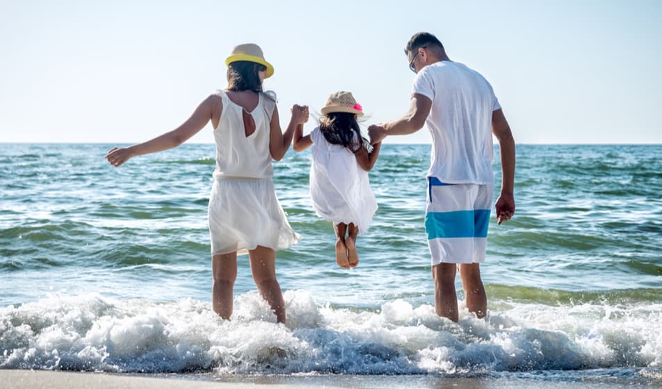 A man and a woman lifting their child above the ocean waves as they go in for a paddle.