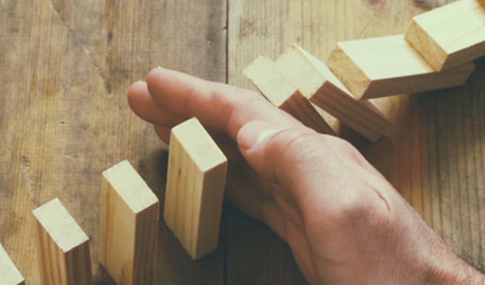 A hand is knocking over wooden dominos. Four dominos have already collapsed on the hand and four are about to be knocked over.