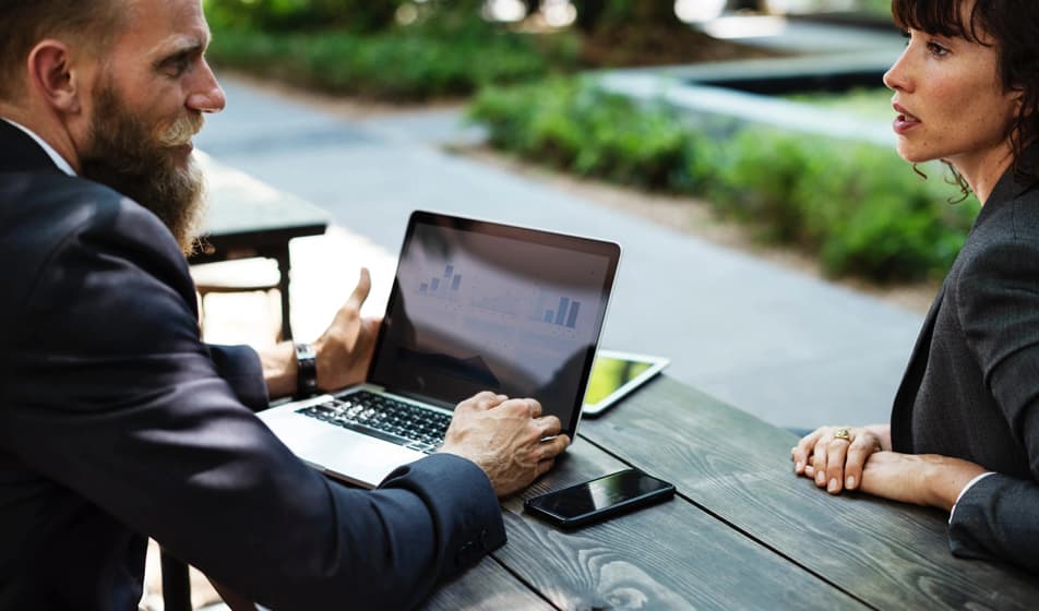 Man working on a laptop talking to a woman on a bench
