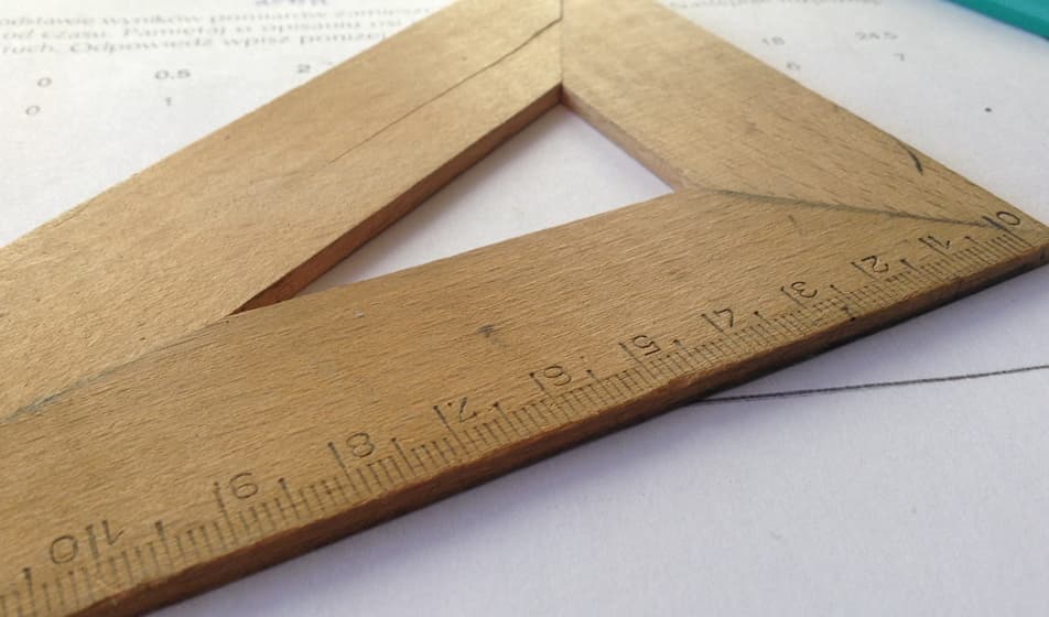 A wooden triangle shaped ruler is on a white piece of paper.