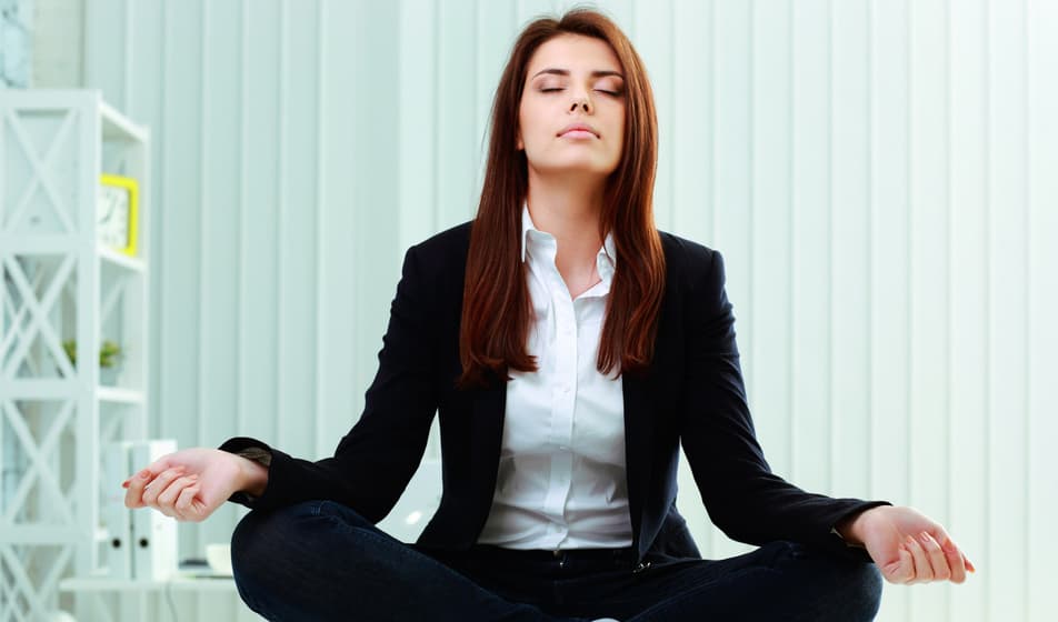 Young beautiful businesswoman meditates on the table in office
