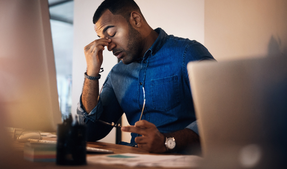 Stressed male employee with head in hand at his desk, showing the psychological impact of redundancy survivor syndrome on surviving employees.