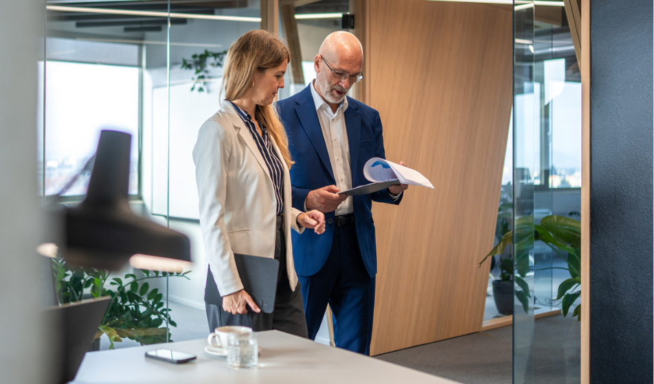 Two workers are walking through an office space with a clipboard, performing a risk assessment for their small business. 
