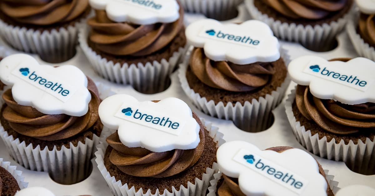 An image of several chocolate cupcakes with swirling chocolate icing. Each cupcake is topped with a cloud shaped Breathe logo.