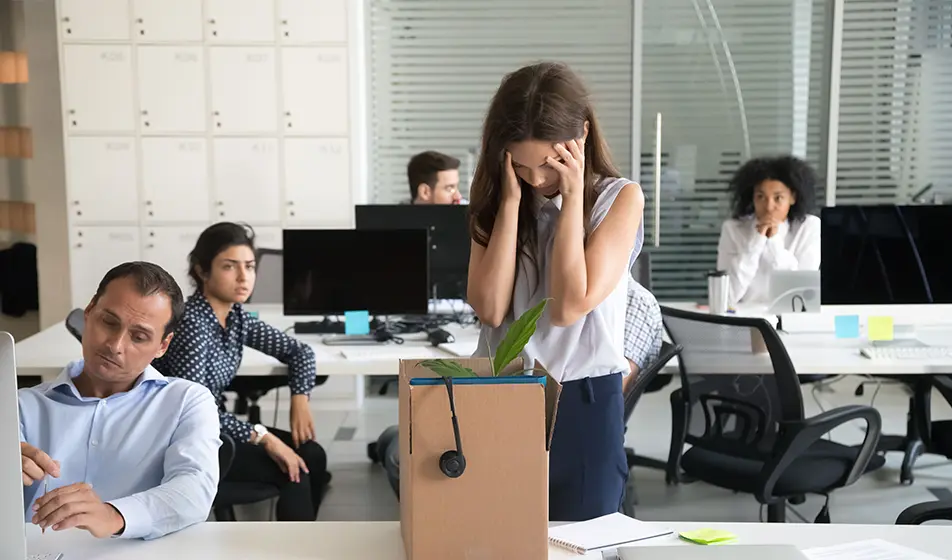 A woman wearing a white shirt is packing away her things from the office. This woman has received a dismissal from her workplace.