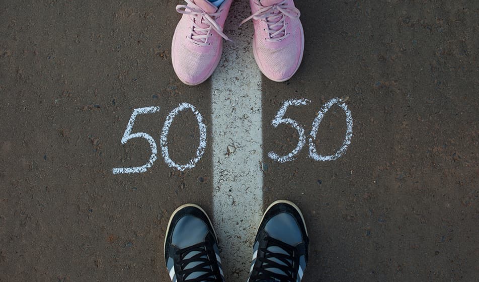 A thick white line has been painted onto concrete in the centre of the image. At the top of the white line are two pink shoes. At the bottom of the white line are two blue shoes. On either side of the line, the number 50 has been written.