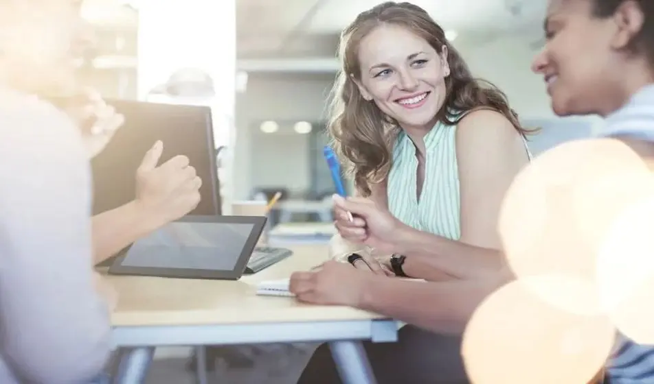 A woman smiling at her colleague as they work around a desk together.