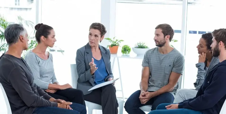 Colleagues are sitting on chairs in a circle and having a group therapy session to promote employee wellbeing.