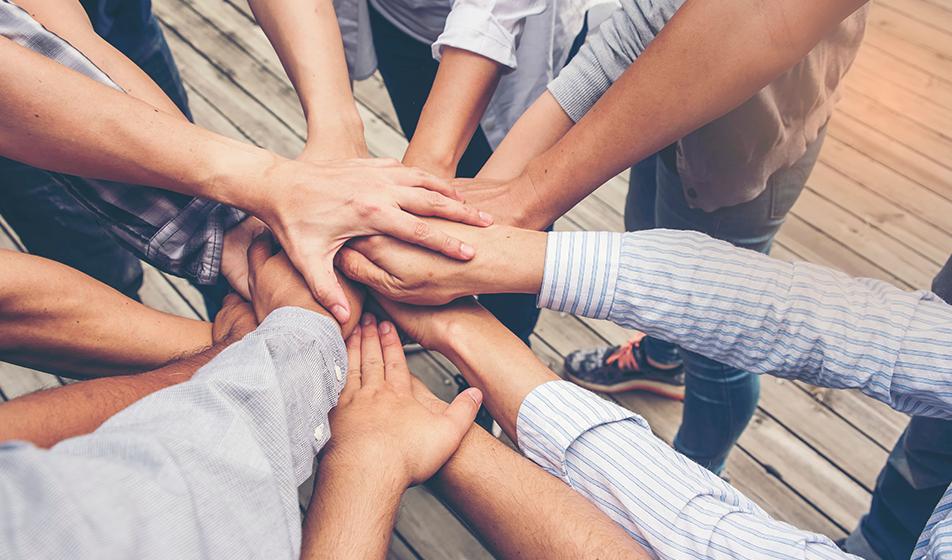 A group of several people in a circle and putting their hands in the centre together.