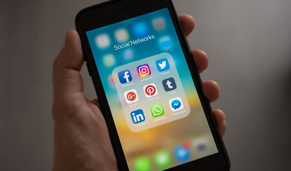 A person is holding a phone which is displaying the different social media apps that are downloaded onto it.