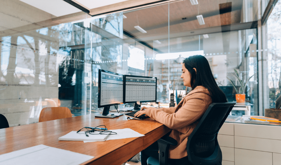 A small business owner working across two monitors displaying spreadsheets, as one of the clearest signs it's time to stop using spreadsheets for HR.