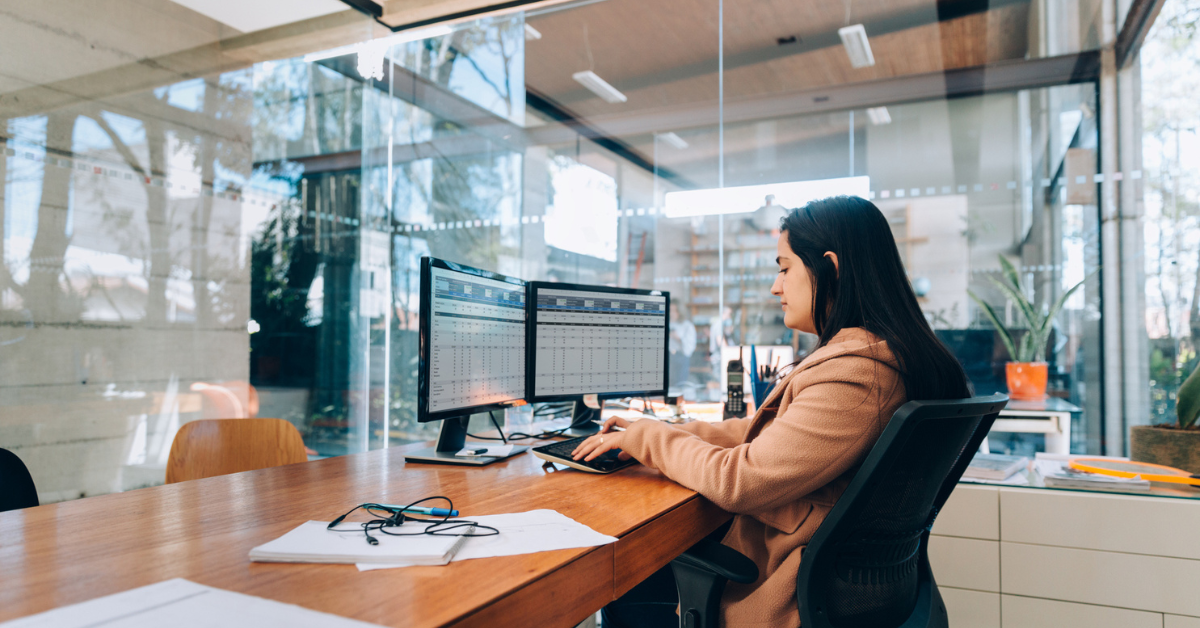 A small business owner working across two monitors displaying spreadsheets, as one of the clearest signs it's time to stop using spreadsheets for HR.
