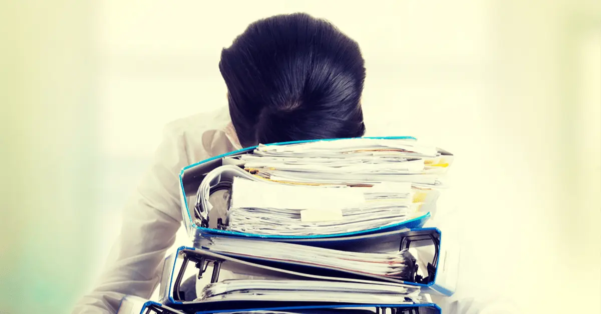 A stressed businesswoman is resting her head on a pile of blue work folders.