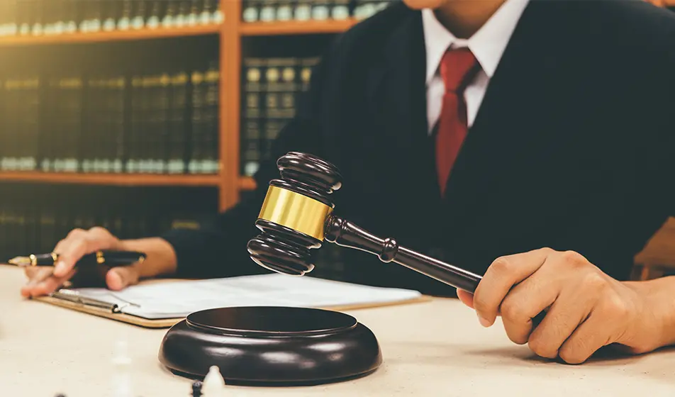 A tribunal is being held. A man has a clipboard in front of him and is holding a gavel in his hand.