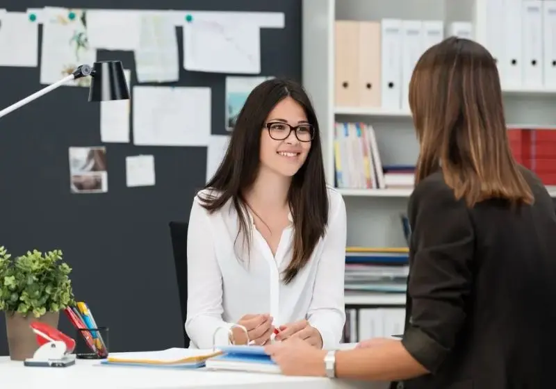Two young businesswomen having a meeting in the office sitting at a desk having a discussion with focus to a young woman wearing glasses (1) (1)