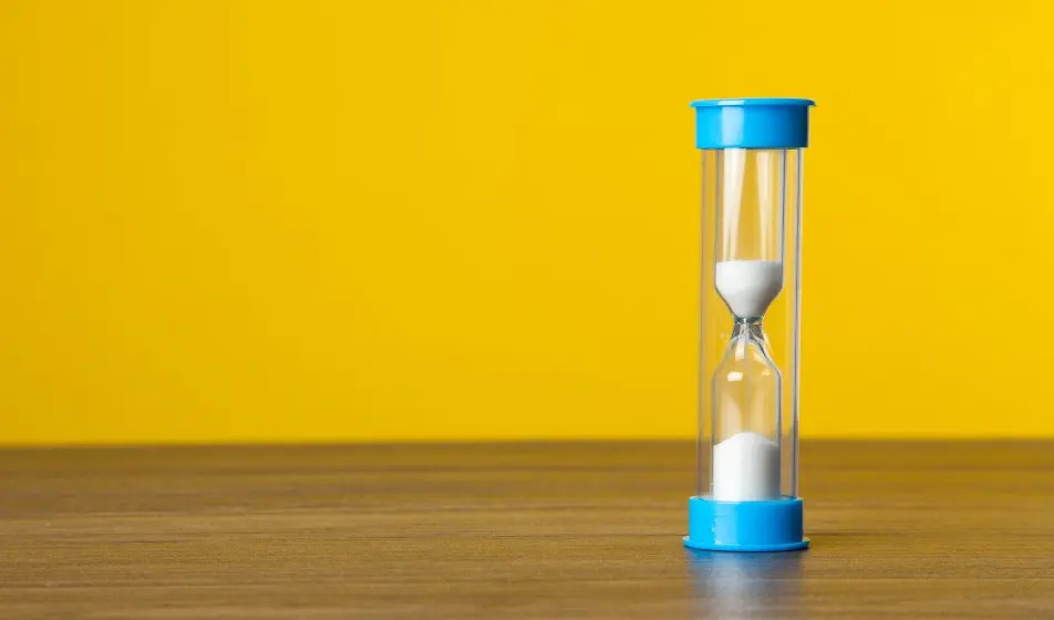Sand timer on a table, with a bright yellow background 