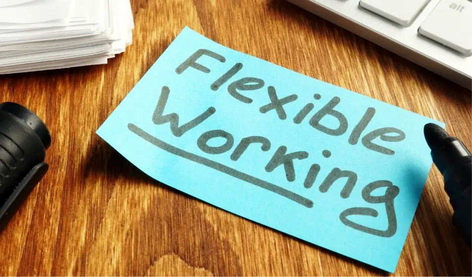 "Flexible working" written on a sticky note, surrounded by a pen, paper, and a keyboard on a desk