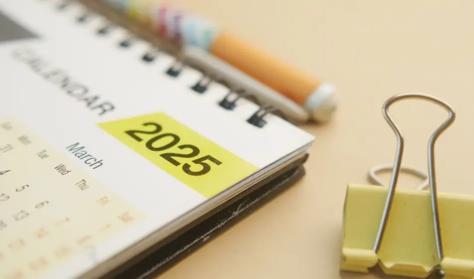 2025 calendar opened at March, 2025 in bold with yellow colour behind it, there is a large plastic paperclip beside it