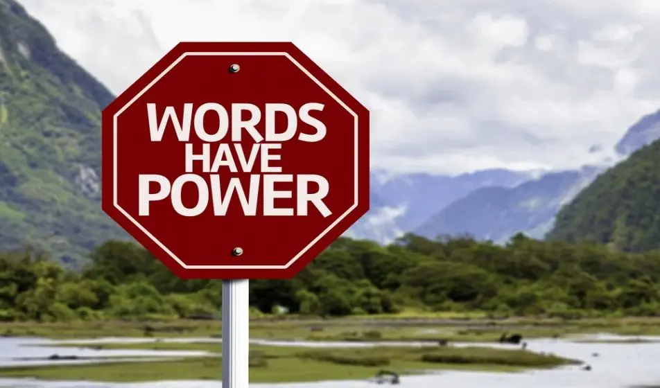 A large red octagon-shaped sign is surrounded by mountains. The sign has "words have power" written on it in white capital letters.