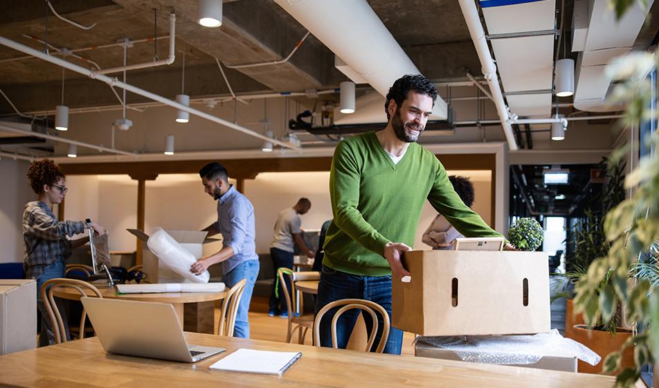 Employees in an office environment are moving boxes of their belongings into a new office space