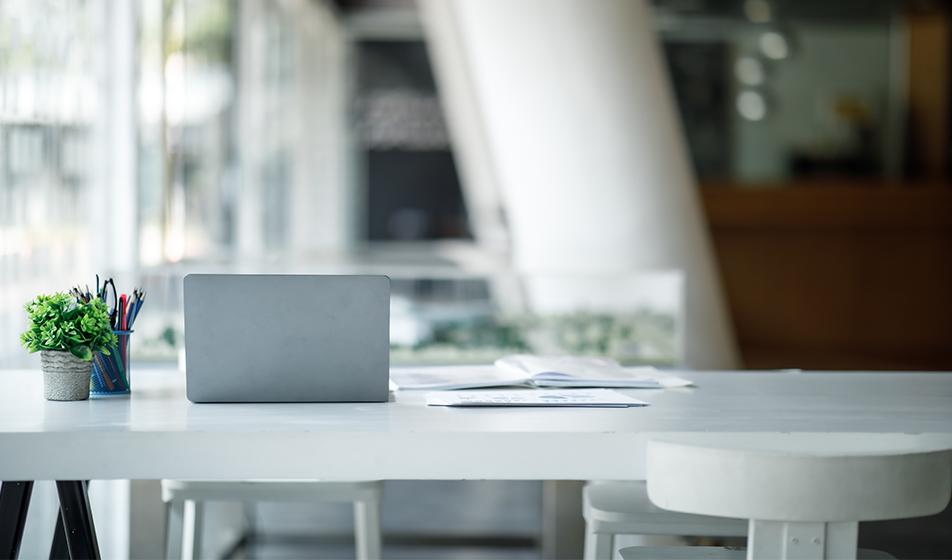 An empty office environment is shown, with a desk, stool and laptop in view. 